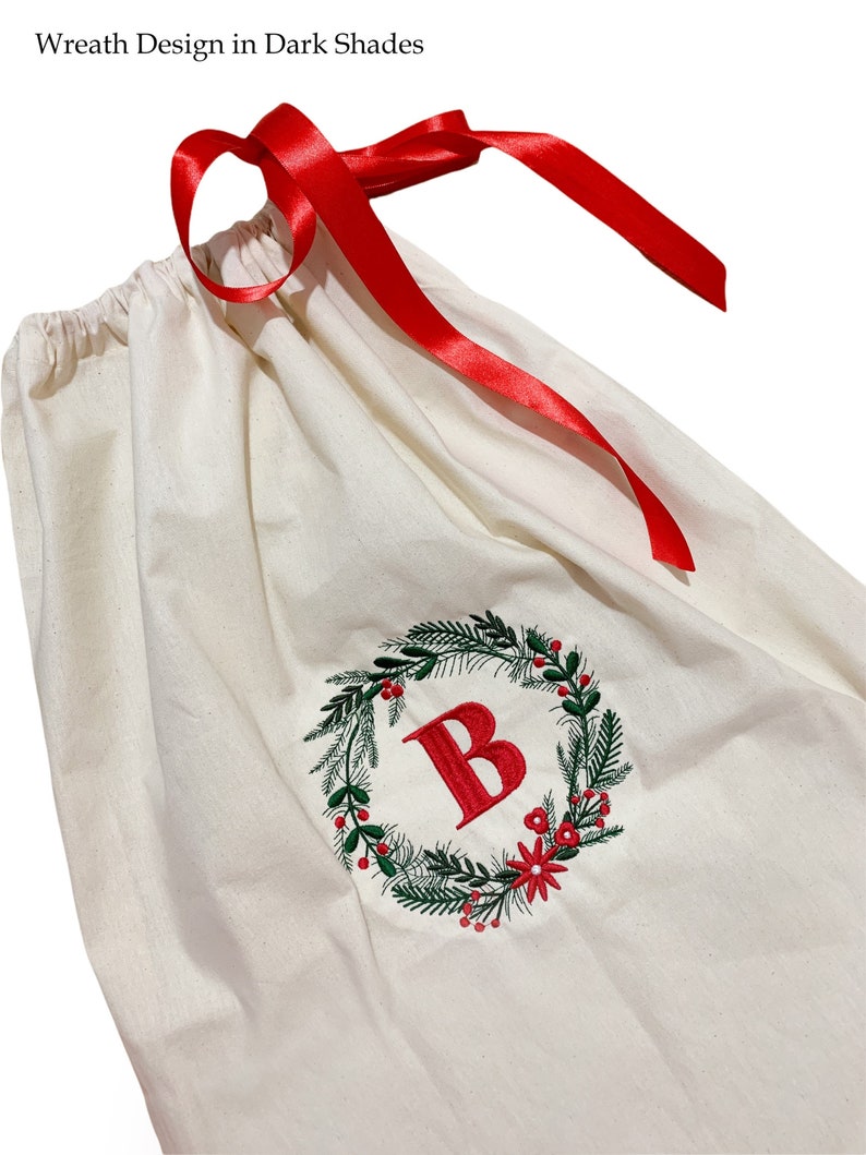 May include: A white canvas gift bag with a red ribbon and a green and red embroidered wreath with the letter "B" in the center.