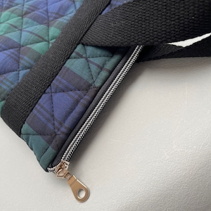 May include: A black and green plaid tote bag with a black strap and a gold zipper pull.