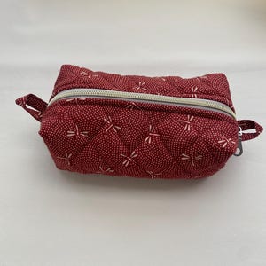 May include: A red quilted zippered pouch with a white dragonfly pattern.