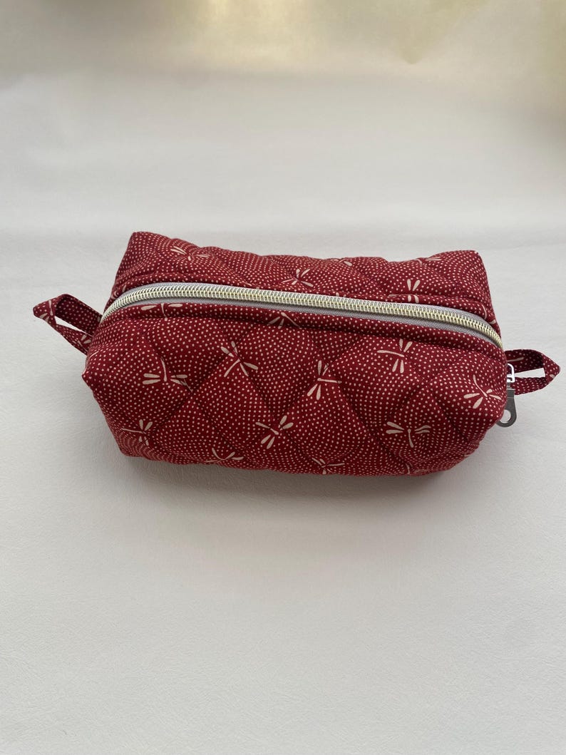 May include: A red quilted zippered pouch with a white dragonfly pattern.