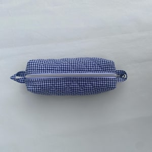Op de afbeelding: Een blauw en wit geruit etui met ritssluiting. De rechthoekige etui heeft een zilveren ritssluiting en kleine stoffen lussen aan elk uiteinde. De etui ligt op een witte ondergrond.