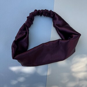 May include: A dark purple satin headband for hair. The headband is made of soft, smooth fabric and is designed to be comfortable to wear.