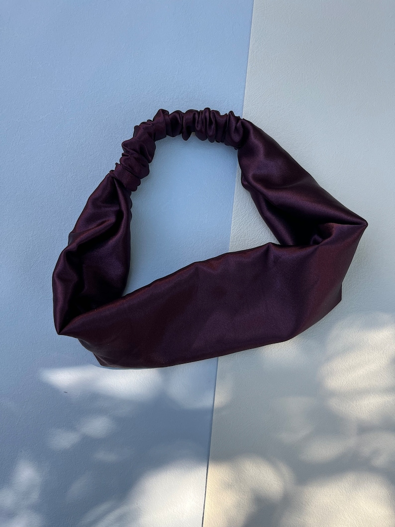 May include: A dark purple satin headband for hair. The headband is made of soft, smooth fabric and is designed to be comfortable to wear.