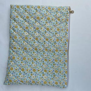 May include: A quilted fabric sleeve with a floral pattern in shades of blue, yellow, and white. The sleeve has a diagonal stitched pattern and a gold-colored zipper closure. The item is likely designed to hold a tablet or laptop.
