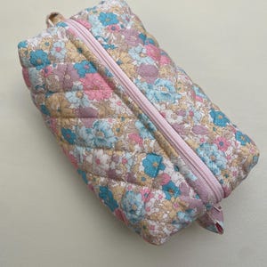 Op de afbeelding: Een quilted toilettas met bloemenprint en een roze rits.