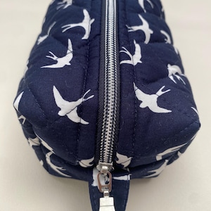 Könnte beinhalten: Eine dunkelblaue, gesteppte Kosmetiktasche mit Reißverschluss und einem weißen Schwalbenmuster. Der Reißverschluss hat einen silbernen Schieber.
