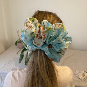 Puede incluir: Un scrunchie para el pelo con estampado floral azul y blanco.