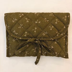 May include: A quilted, olive green wrap with a dragonfly and dot pattern. The wrap is tied with a matching fabric tie. The dragonfly design is in a cream color.