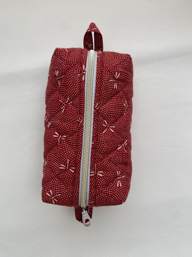 May include: A red quilted zippered pouch with a white dragonfly pattern. The pouch has a top handle and a zipper closure.