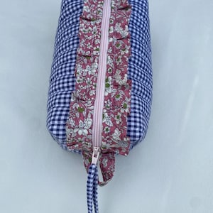 May include: A rectangular pencil case with a blue and white gingham pattern. The pink zip is central, flanked by a floral print panel on a pink background. A matching fabric pull and bow complete the design.