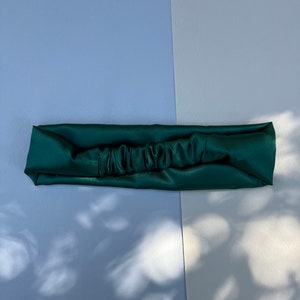May include: A dark green satin headband with a gathered detail in the centre.
