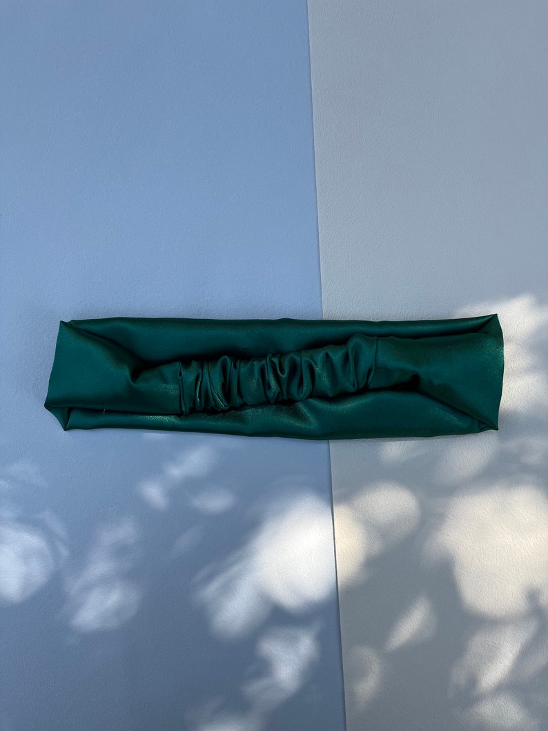 May include: A dark green satin headband with a gathered detail in the centre.