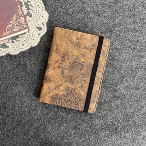 May include: A brown leather notebook cover with a floral embossed design and a black elastic closure.