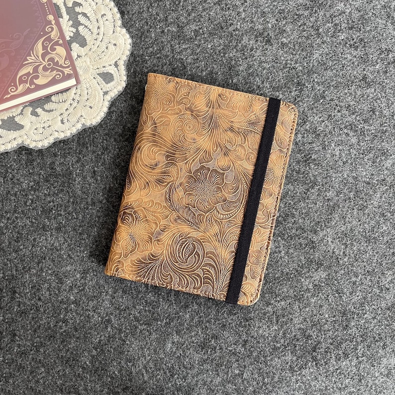 May include: A brown leather notebook cover with a floral embossed design and a black elastic closure.