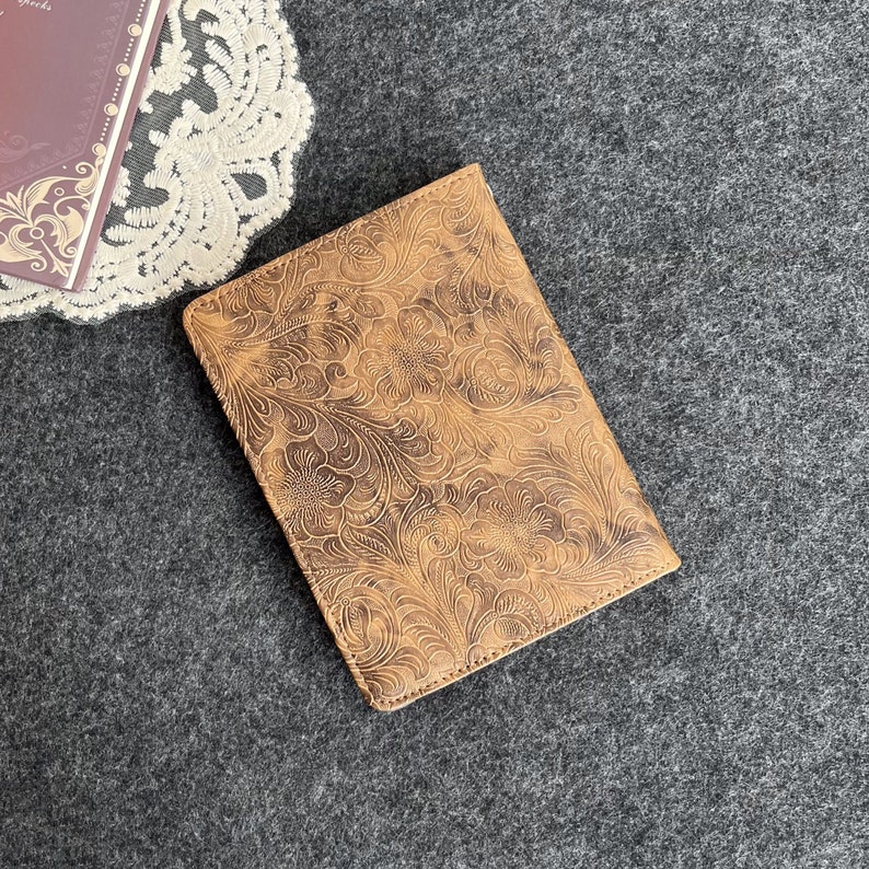 May include: A brown leather notebook cover with an embossed floral pattern. The cover has a distressed look and is made of a soft, supple leather.