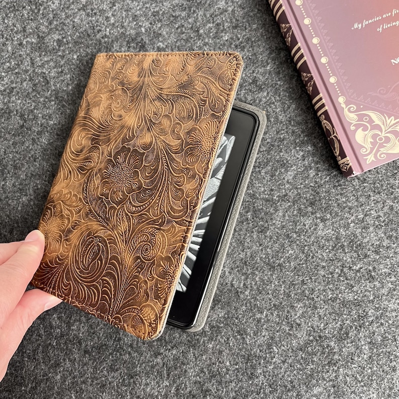 May include: A brown leather e-reader case with an embossed floral pattern. The case is open and an e-reader is visible inside.