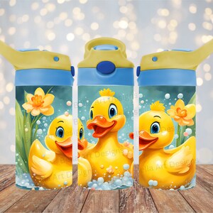 Puede incluir: Tres patos de goma amarillos con ojos azules y picos naranjas se muestran sobre un fondo azul y verde con burbujas blancas. Los patos est&aacute;n en una escena de agua con un narciso amarillo. La imagen est&aacute; en una botella de agua azul y amarilla con una tapa azul y un pico amarillo.