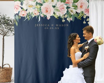 May include: A navy blue backdrop with a floral design of pink and white roses and greenery. The text "JESSICA & MASON 09.26.XX" is printed in gold. A couple is embracing in front of the backdrop.