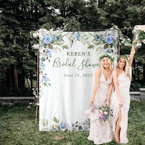 Pode incluir: Um fundo branco com desenhos florais de aquarela azul e verde. O texto "Keren's Bridal Shower June 25, 2022" está impresso no fundo. Duas pessoas estão em pé na frente do fundo.