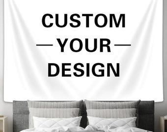 Può includere: Arazzo bianco con testo nero che recita "CUSTOM - YOUR - DESIGN". L'arazzo è appeso a una parete dietro un letto con biancheria da letto bianca e cuscini grigi.