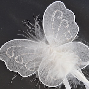 May include: White butterfly wings with silver glitter accents and a white feather centre. The wings are made of a sheer fabric and are attached to a white stick.