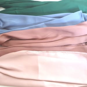 May include: Four different coloured scarves stacked on top of each other. The top scarf is green, the second is blue, the third is pink, and the bottom scarf is a light pink.