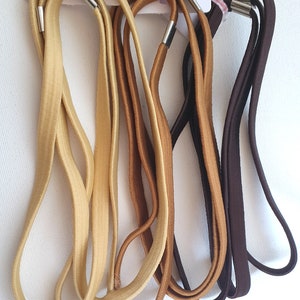 May include: A selection of hair ties in gold, brown, and dark brown. Each tie features a silver-coloured metal clasp and is held together with a pink elastic band. The ties are presented against a white backdrop.