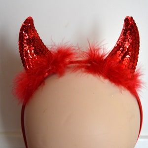 May include: Red devil horns headband with red feathers. The headband is made of a thin, flexible material and is designed to fit comfortably on the head.
