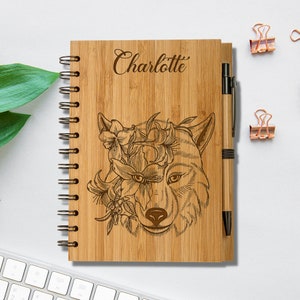 May include: A personalized bamboo notebook with a wolf and flowers design. The notebook has a spiral binding and a matching pen. The name "Charlotte" is engraved on the front cover.