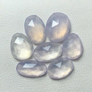 Könnte beinhalten: Acht facettierte, ovale, durchscheinende, hellviolette Edelsteine. Die Steine haben eine leicht irisierende Qualität.