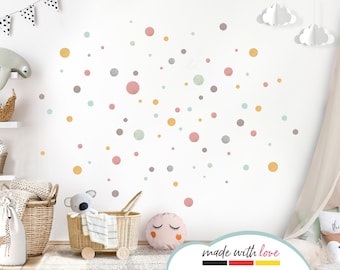 May include: A white wall adorned with pastel-coloured polka dot wall stickers in pink, yellow, grey, and blue. The room is decorated with children's toys and accessories, including a koala bear and a basket.