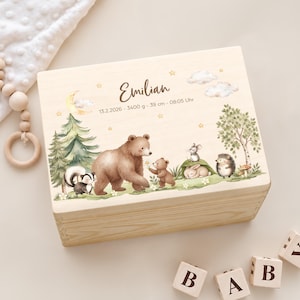 Könnte beinhalten: Eine rechteckige Holzkiste mit einem aufgedruckten Waldmotiv, das einen Bären, ein Stinktier, eine Maus, einen Hasen und einen Igel zeigt. Der Text lautet Emilian, 13.2.2026 - 3400 g - 39 cm - 08:05 Uhr, ergänzt durch Mond, Sterne und Wolken.