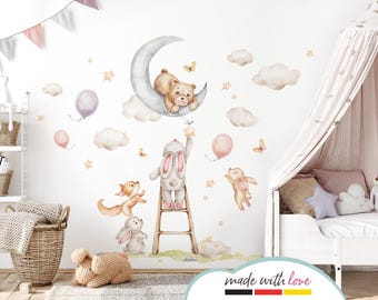 May include: A set of watercolor-style wall decals featuring a brown bear sleeping on a crescent moon, a gray bunny climbing a ladder, a fox, and a bunny with outstretched arms. The decals are surrounded by clouds, stars, and balloons.
