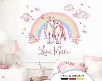 Könnte beinhalten: Zwei weiße Einhörner mit rosa Mähnen und Schwänzen stehen zusammen vor einem Regenbogen. Die Einhörner sind von rosa Blumen und Schmetterlingen umgeben. Der Text "Lena Marie" steht unter den Einhörnern.