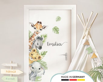 May include: A white door with a watercolor animal decal featuring a giraffe, zebra, lion, and elephant. The decal is surrounded by green leaves and the name "Emilia" is written in cursive. The door has a silver door handle and a sign that reads "Made in Germany".