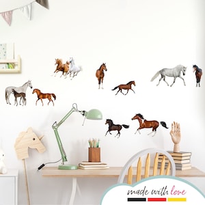 Op de afbeelding: Een witte muur met verschillende paarden silhouetten in verschillende poses en kleuren. De silhouetten zijn in een willekeurig patroon gerangschikt. De muur is versierd met een houten plank en een lamp. De tekst "made with love" staat onderaan de afbeelding.