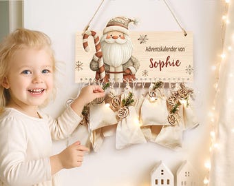 May include: A wooden Advent calendar featuring a Santa Claus illustration, the name "Sophie", and 24 small fabric bags. The calendar is decorated with snowflakes and small wooden ornaments. A young child is smiling and pointing at the calendar.