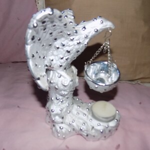 Könnte beinhalten: Silberne Adlerfigur aus Metall mit einer hängenden Schale und einem Kerzenhalter. Der Adler hat eine strukturierte Oberfläche mit kleinen silbernen Punkten.