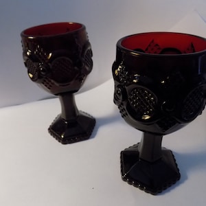 May include: Two dark red glass goblets with a textured design. The goblets have a hexagonal base and a round bowl.
