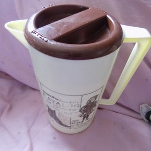 May include: A white plastic pitcher with a brown lid and a yellow handle. The pitcher has a graphic of a man in a hat and the text "Grand Prix -  ITALIA - 1978".