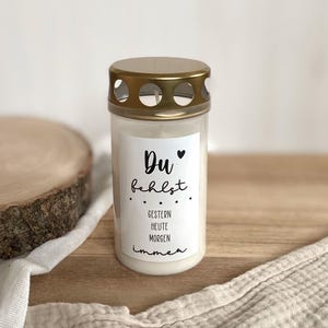 Könnte beinhalten: Eine weiße Kerze mit einem goldenen Deckel und einem schwarzen Etikett mit der Aufschrift "Du fehlst... Gestern Heute Morgen Immer".