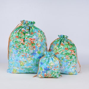 May include: Three drawstring bags in different sizes with a floral pattern on a light blue background. The bags have a brown drawstring.