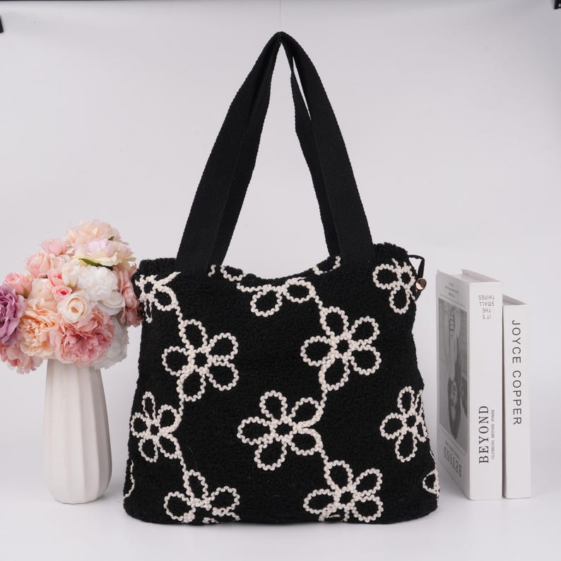 May include: Black tote bag with white embroidered flowers. The bag has two black straps.