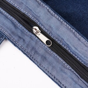 Peut inclure: Gros plan sur un tissu en jean avec une fermeture &eacute;clair noire et un curseur argent&eacute;. La fermeture &eacute;clair est partiellement ouverte, r&eacute;v&eacute;lant les dents. Le denim est bleu moyen avec des accents bleu clair et des coutures blanches.