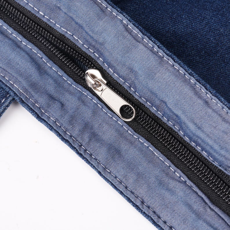 Peut inclure: Gros plan sur un tissu en jean avec une fermeture &eacute;clair noire et un curseur argent&eacute;. La fermeture &eacute;clair est partiellement ouverte, r&eacute;v&eacute;lant les dents. Le denim est bleu moyen avec des accents bleu clair et des coutures blanches.