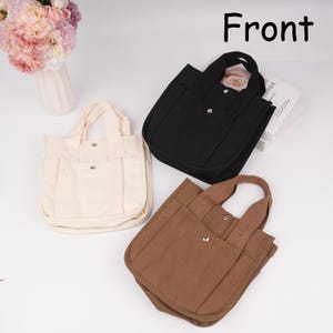 Pode incluir: Tr&ecirc;s pequenas bolsas tote de lona nas cores creme, preta e castanha. Cada bolsa possui duas al&ccedil;as, um bolso frontal com fecho de bot&atilde;o de press&atilde;o em metal prateado e um compartimento principal. A palavra Front est&aacute; impressa a preto no canto.