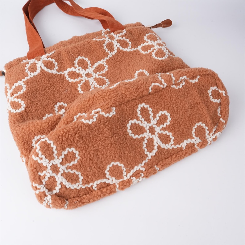May include: A brown tote bag with white embroidered flowers. The bag is made of a soft, fuzzy material.
