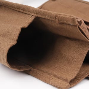 Pode incluir: Uma bolsa utilit&aacute;ria de lona castanha com m&uacute;ltiplos compartimentos abertos e bordas costuradas refor&ccedil;adas. O tecido tem uma textura tecida vis&iacute;vel e o design inclui bolsos estruturados destinados a manter v&aacute;rios itens no lugar com seguran&ccedil;a.