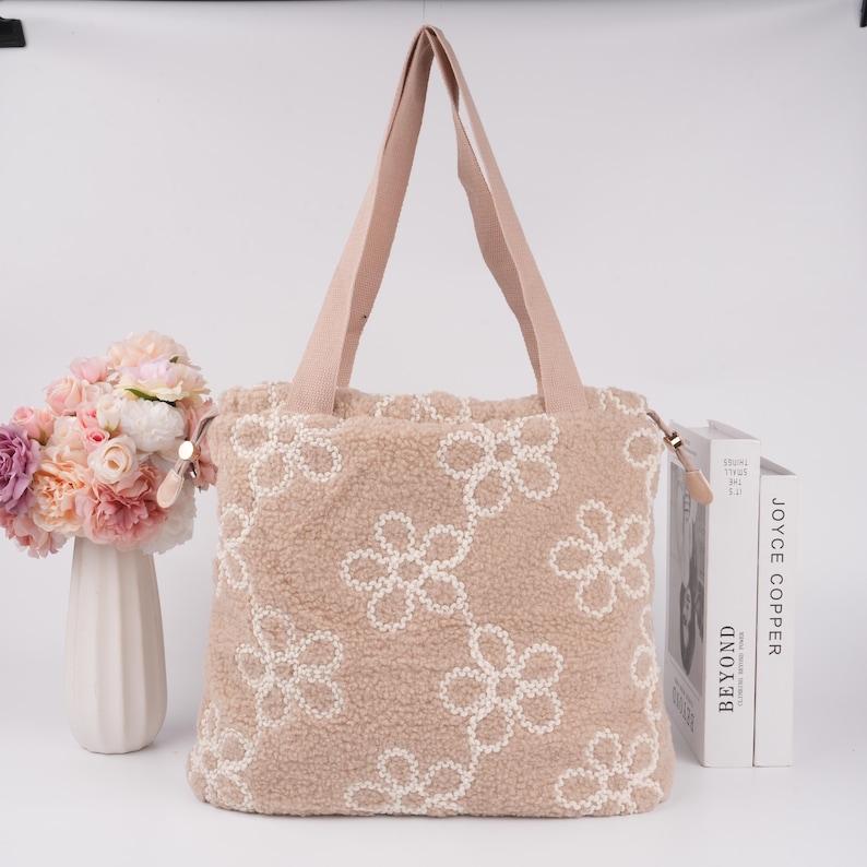 May include: A beige tote bag with a fuzzy texture and white embroidered flower designs. The bag has two long straps.