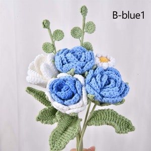 May include: A bouquet of crocheted flowers in shades of blue and white. The bouquet includes three blue roses, one white rose, and one white daisy with a yellow center. The flowers are attached to green crocheted stems and leaves.